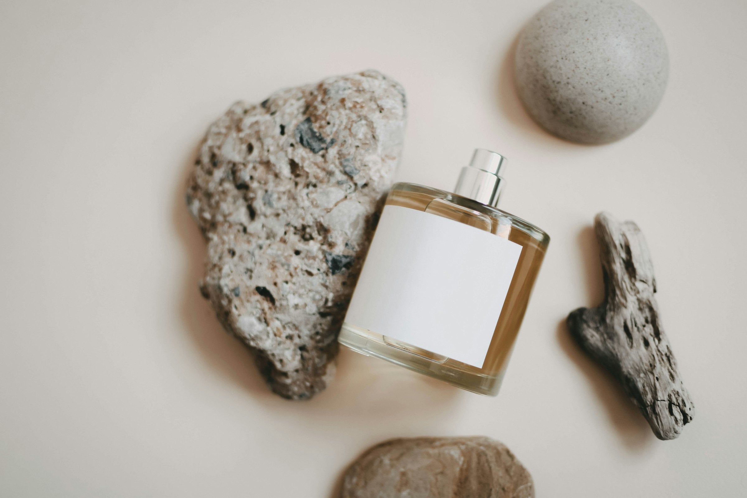 Perfume bottle with blank label flat-lay on cream surface with natural stones and driftwood